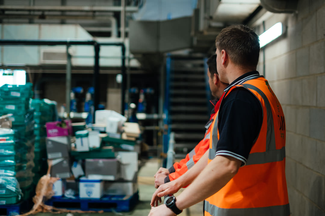 Ricky & Kyrone from ONM energy stand in orange high vis vests overlooking a waste reception area of an AD plant